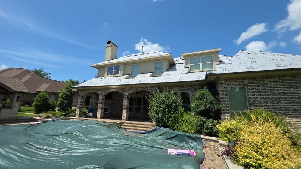 Residential home with new roof installation and landscaping under clear blue sky.