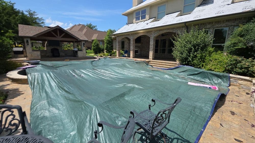 Green tarp covering a backyard pool area next to a stone patio and house.