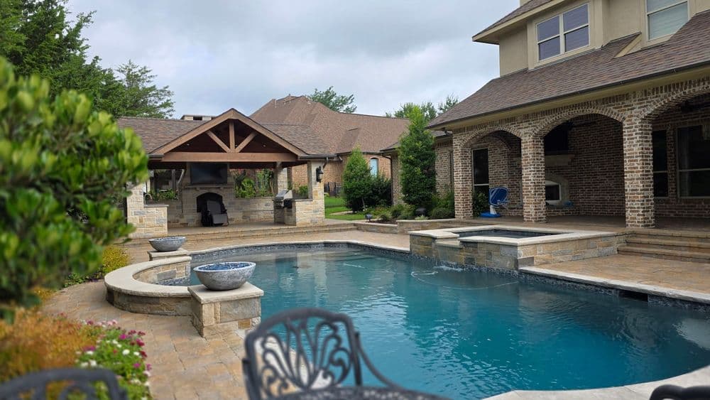 Luxury backyard with a pool, spa, and outdoor kitchen under a covered patio.